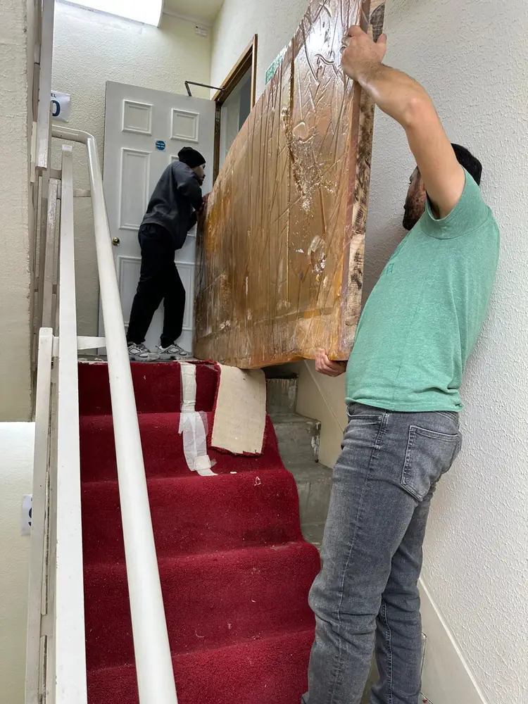 Two movers carrying a wrapped headboard upstairs